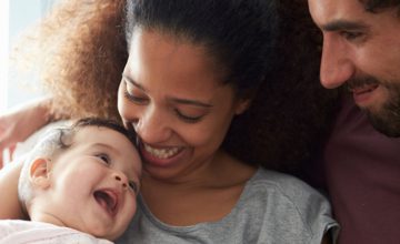 Two adults cuddle a smiling baby