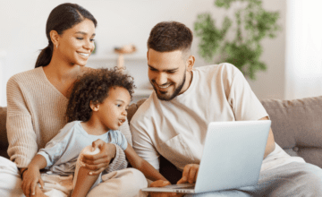 parents and baby look at laptop sitting on couch
